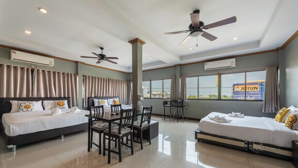 Une chambre d’hôtel avec deux lits, une table à manger, des chaises, des ventilateurs de plafond, de grandes fenêtres et des climatiseurs.