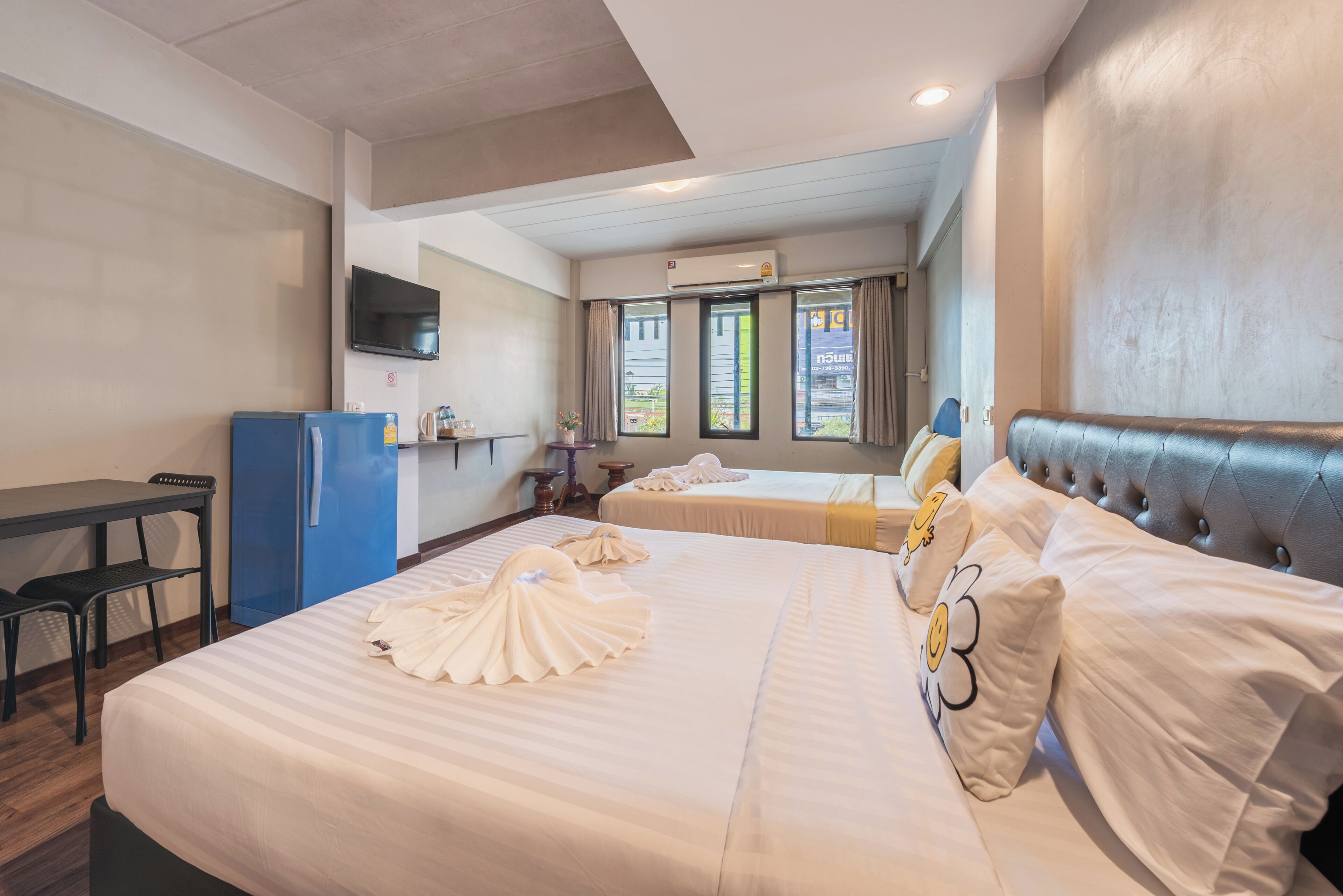 A hotel room with two beds, a desk, a television, and an air conditioning unit.