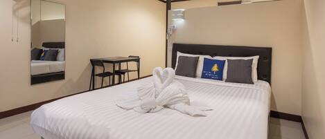 A hotel room with a bed, a mirror, a desk, and a fan.