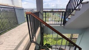 Un escalier avec des marches en bois et des rampes en métal, menant à un balcon extérieur d’où l’on peut admirer la verdure.
