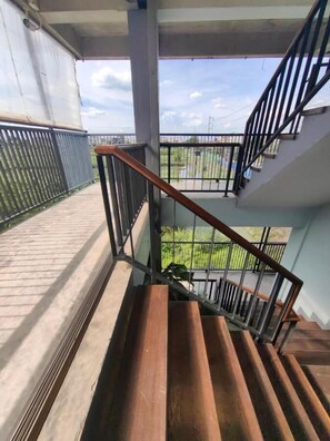 Una escalera de madera con barandillas de metal que conduce a un balcón exterior con vistas a zonas verdes.
