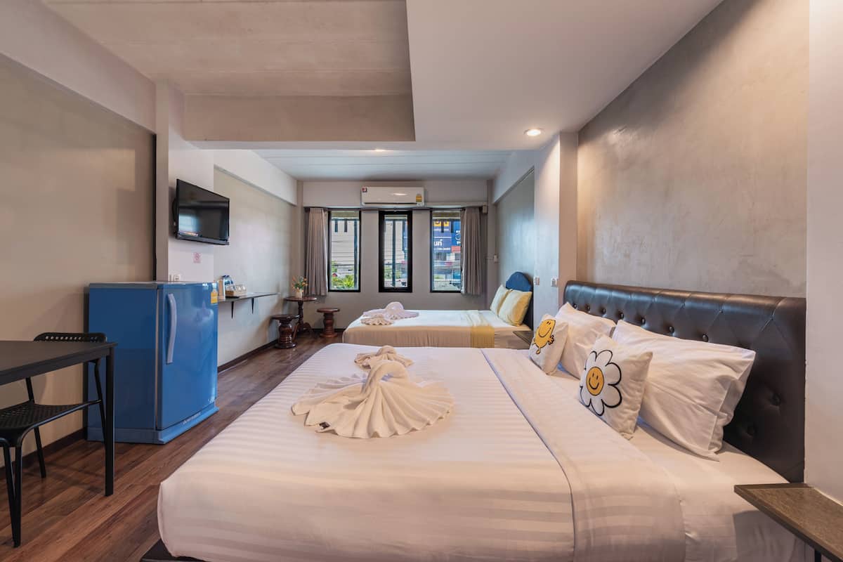 Quarto de hotel com cama, escrivaninha, frigorífico azul e televisão na parede.