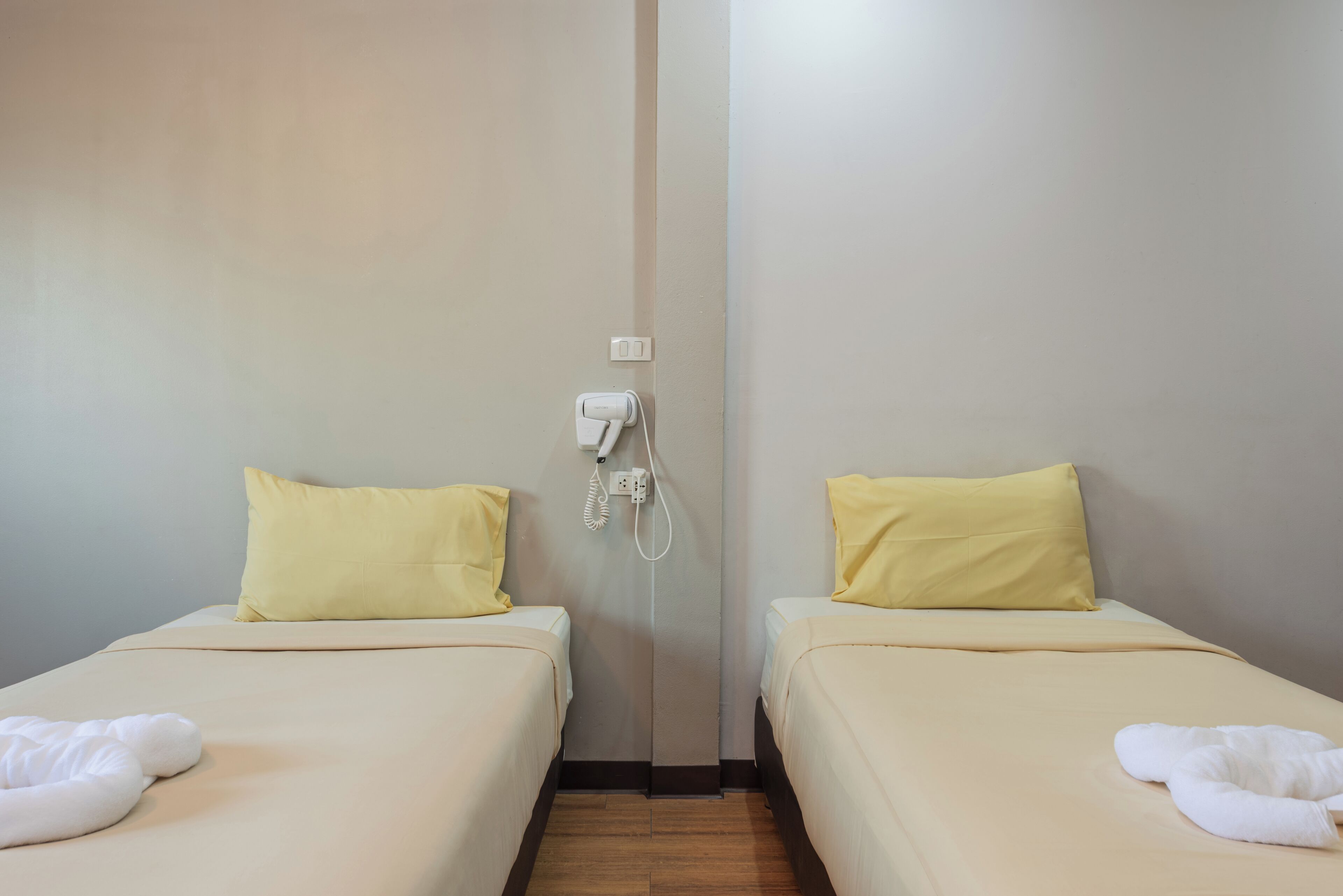 Una camera d'albergo con due letti, ognuno con un cuscino giallo e un asciugamano bianco.