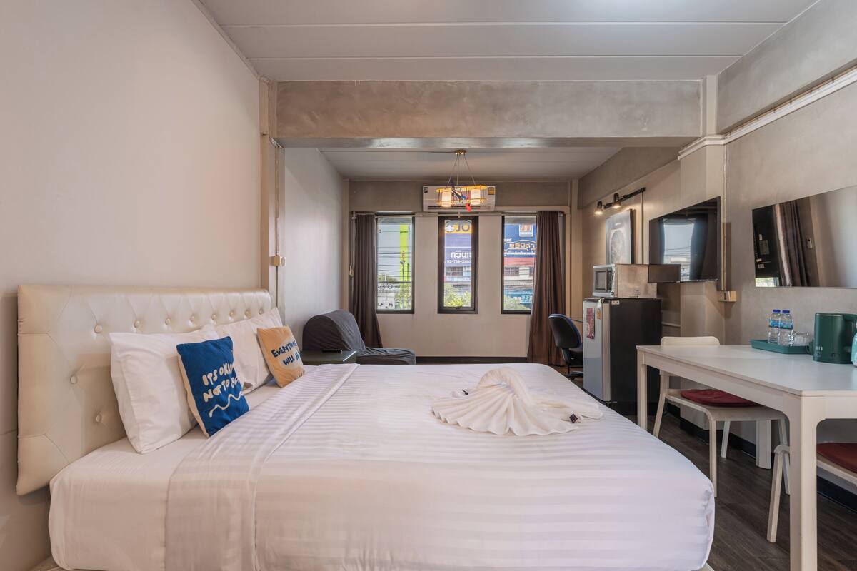 Quarto de hotel com cama, escrivaninha, cadeira, televisão e minibar.