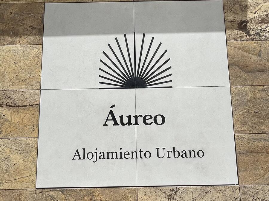 Letrero que dice "Áreo Alojamiento Urbano" sobre un piso de baldosas.