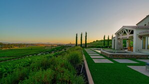 A landscaped garden with a pool, a patio area, and a view of distant hills. - Mansion on De Portola with Vineyard and Mountain view (Temecula)