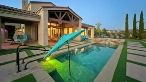 A pool area with a modern house in the background, a clear sky, and a well-maintained lawn. - Mansion on De Portola with Vineyard and Mountain view (Temecula)