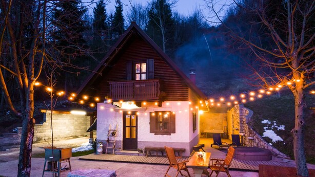 Un chalet confortable avec une façade en pierre, une terrasse en bois et des guirlandes lumineuses.