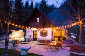 Una cabaña acogedora con fachada de piedra, terraza de madera y luces colgantes.