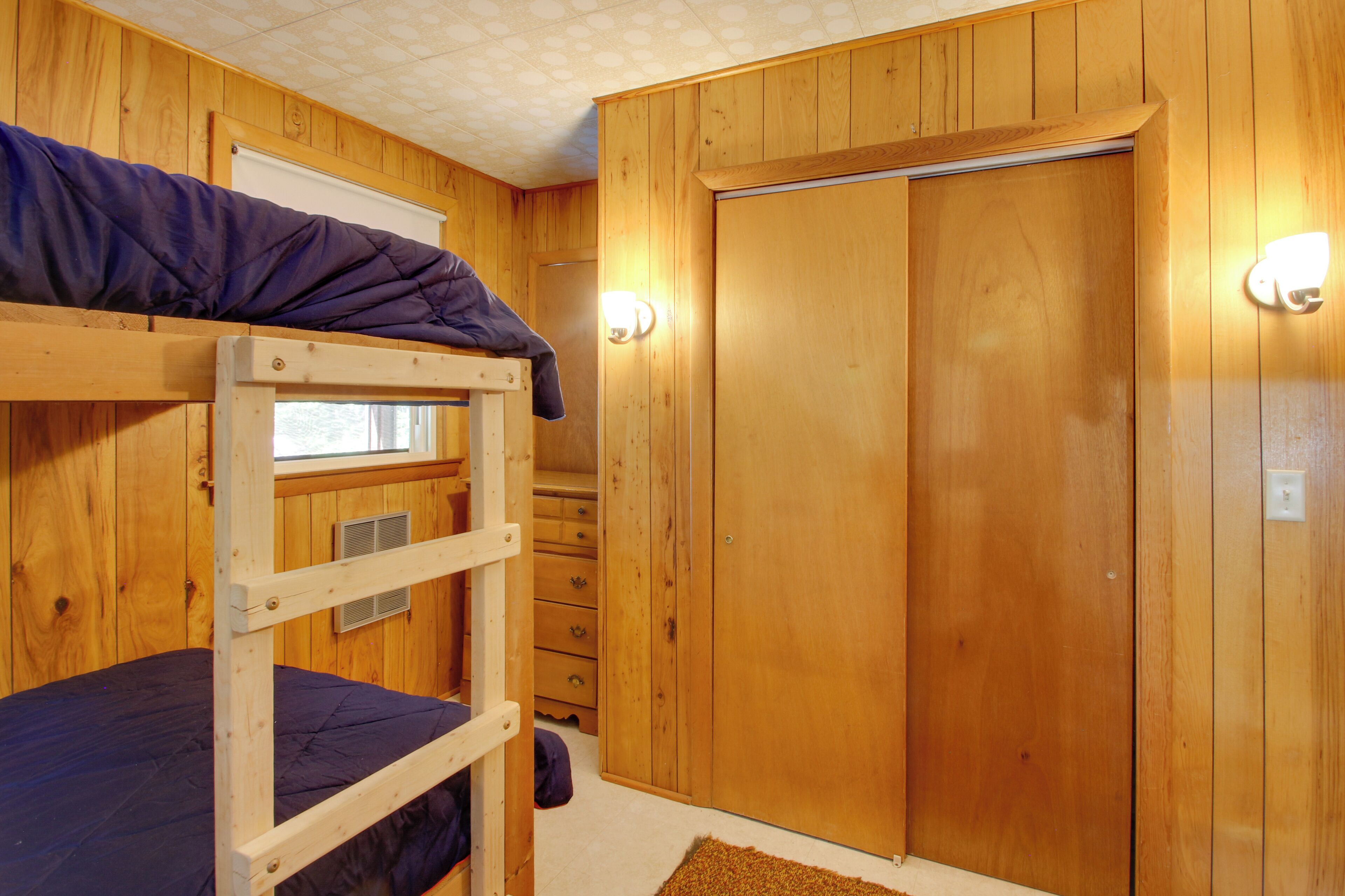 A bunk bed room with wooden walls, a wardrobe, and a window.