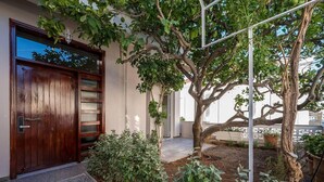 A wooden door with a metal handle, a small garden with various plants, and a tree with a white trellis. - Sofia's Lemontree 3-bed House in Agios Nikolaos (Agios Nikolaos)