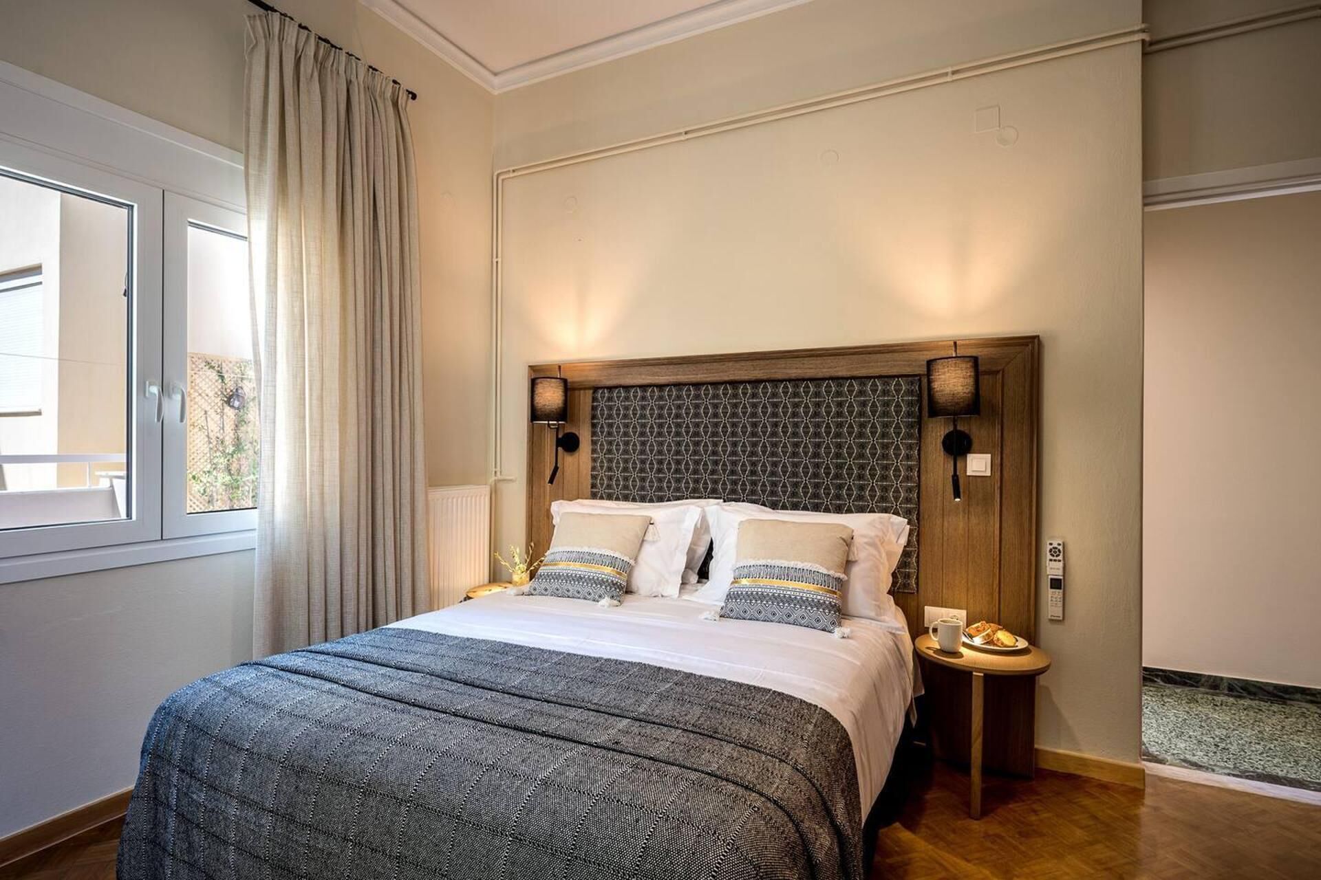 A neatly made bed with a patterned bedspread and pillows, a bedside table with a lamp, and a window with curtains.