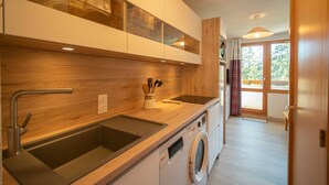 A modern kitchen with wooden cabinetry, a built-in dishwasher, and a large window providing natural light.