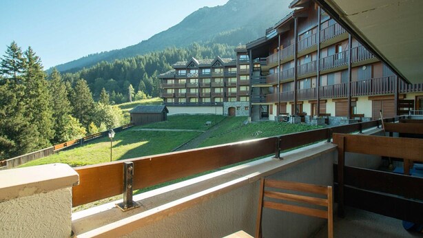 A hotel with multiple balconies, a view of a mountain, and a small building in the foreground.