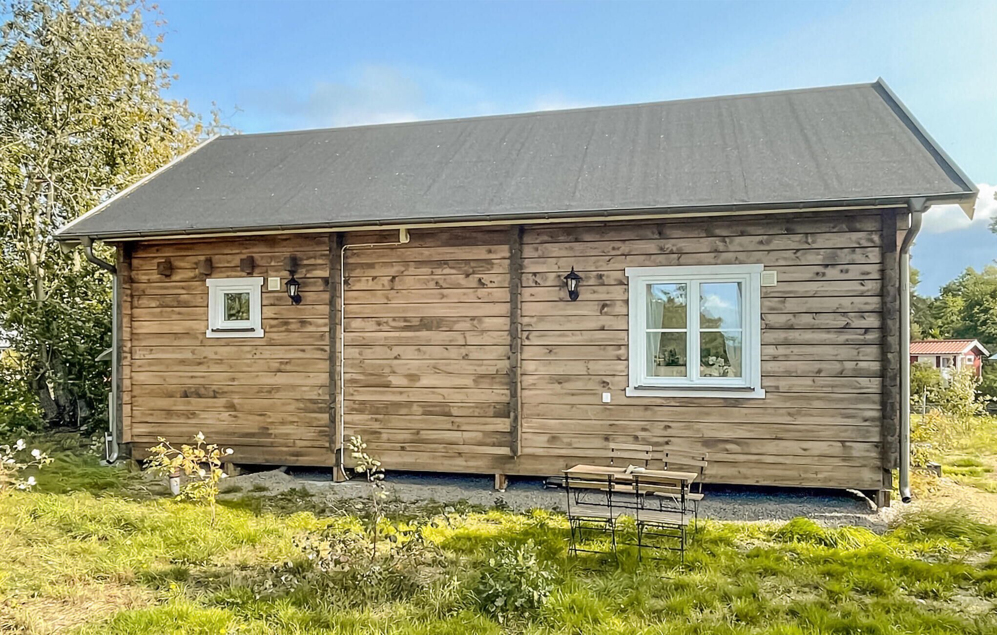 A wooden cabin with a dark roof, two windows, and a bench outside.