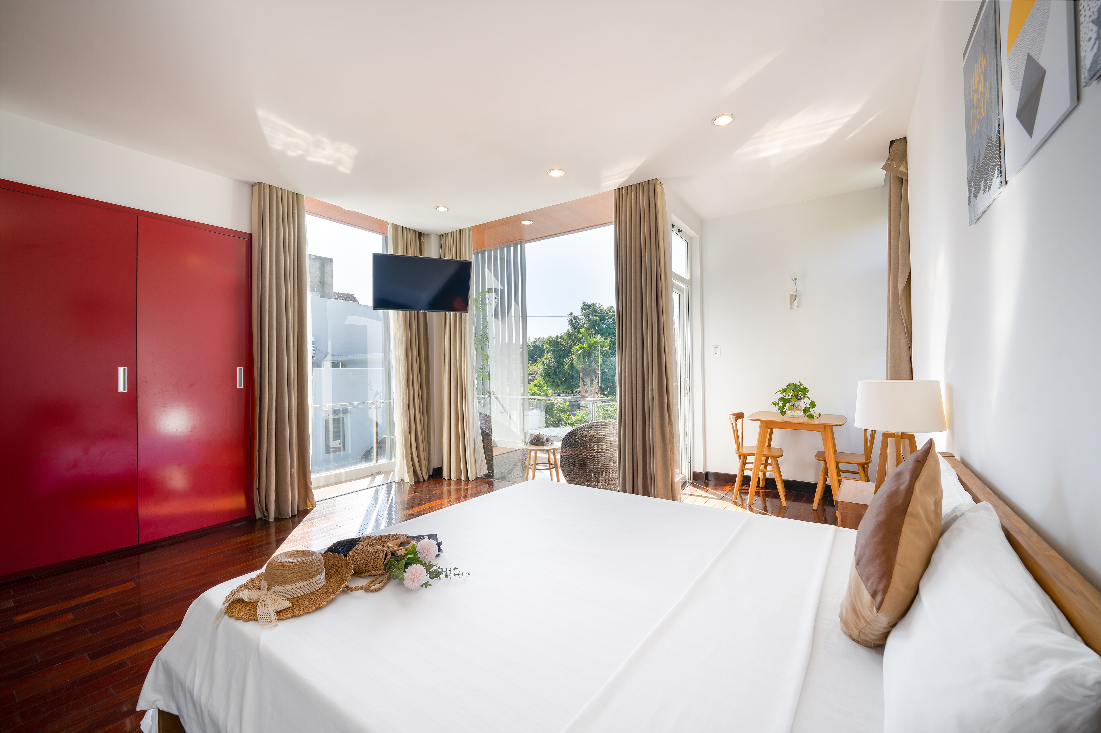 Habitación de hotel con una cama grande, un armario rojo, televisión, balcón con mesa y sillas y vistas a zonas verdes.