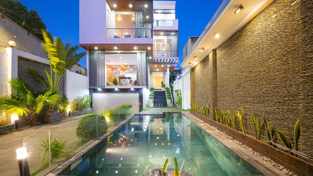 Un área de piscina moderna con una barandilla de cristal, una mesa con bebidas y una escalera que lleva a un balcón en un segundo piso.