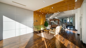 Amplia sala de estar con piso de madera, un sofá verde, una mesa de centro y una escalera que lleva a un nivel superior.