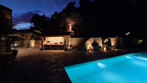 Zona de piscina con estructura de piedra, mobiliario exterior y pared de piedra.
