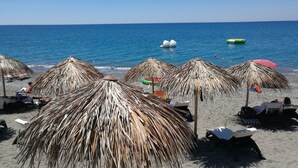 Una playa con sombrillas de paja y sillas reclinables.