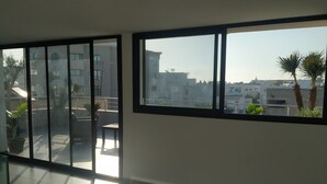 Um quarto amplo com grandes janelas que oferecem vista para um horizonte urbano e palmeiras.