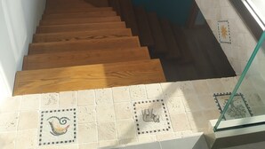 Uma escadaria com degraus de madeira e guarda-corpo de vidro, dando acesso a uma varanda com vista.