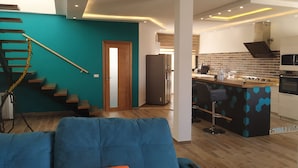 Uma sala de estar moderna com um sofá azul, uma cozinha com área de bar e uma escada com paredes verde-água.