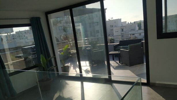 Um apartamento moderno com varanda, grandes janelas e vista para edifícios ao redor.