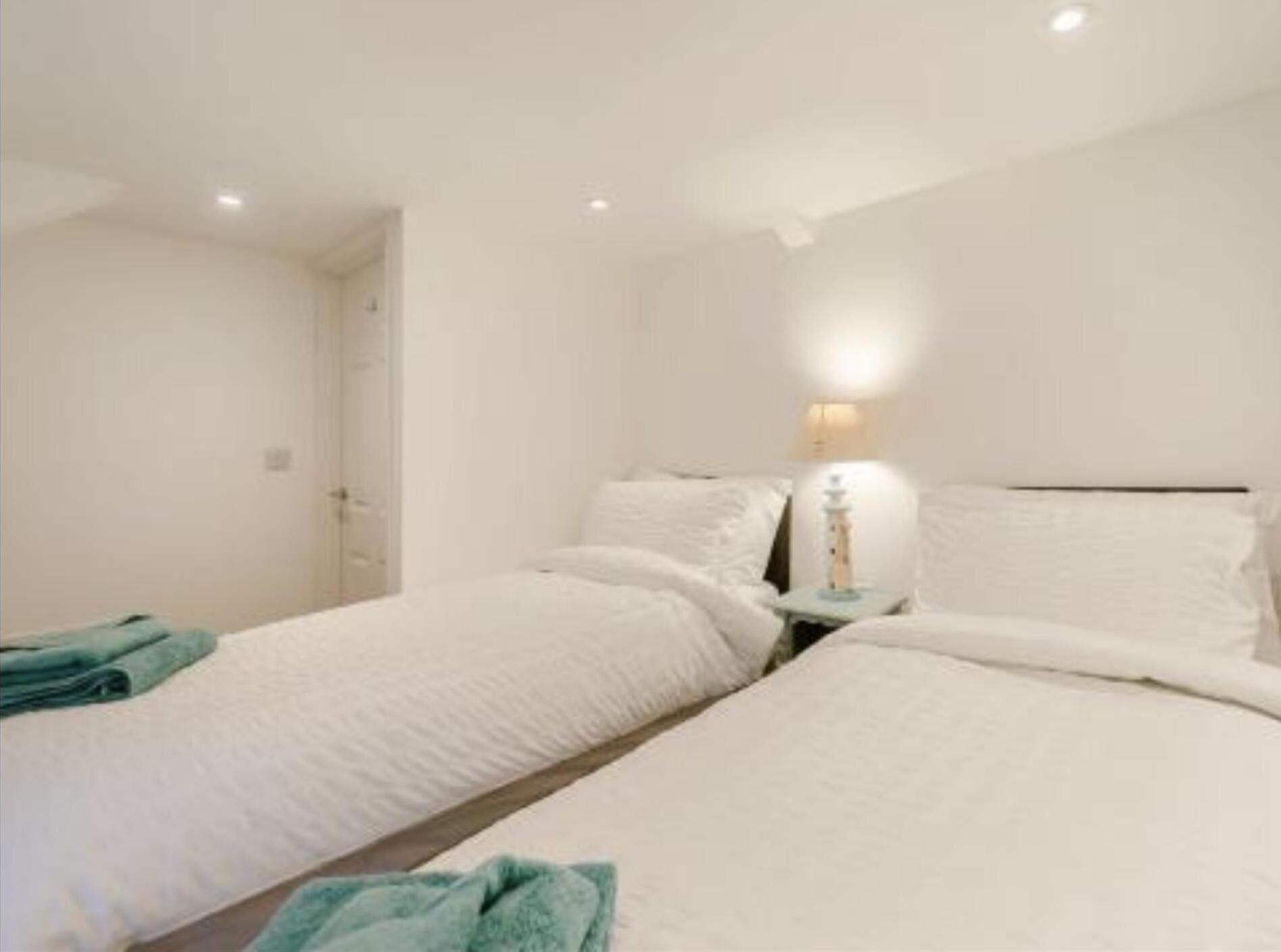 A hotel room with two beds, a bedside table with a lamp, and a door.