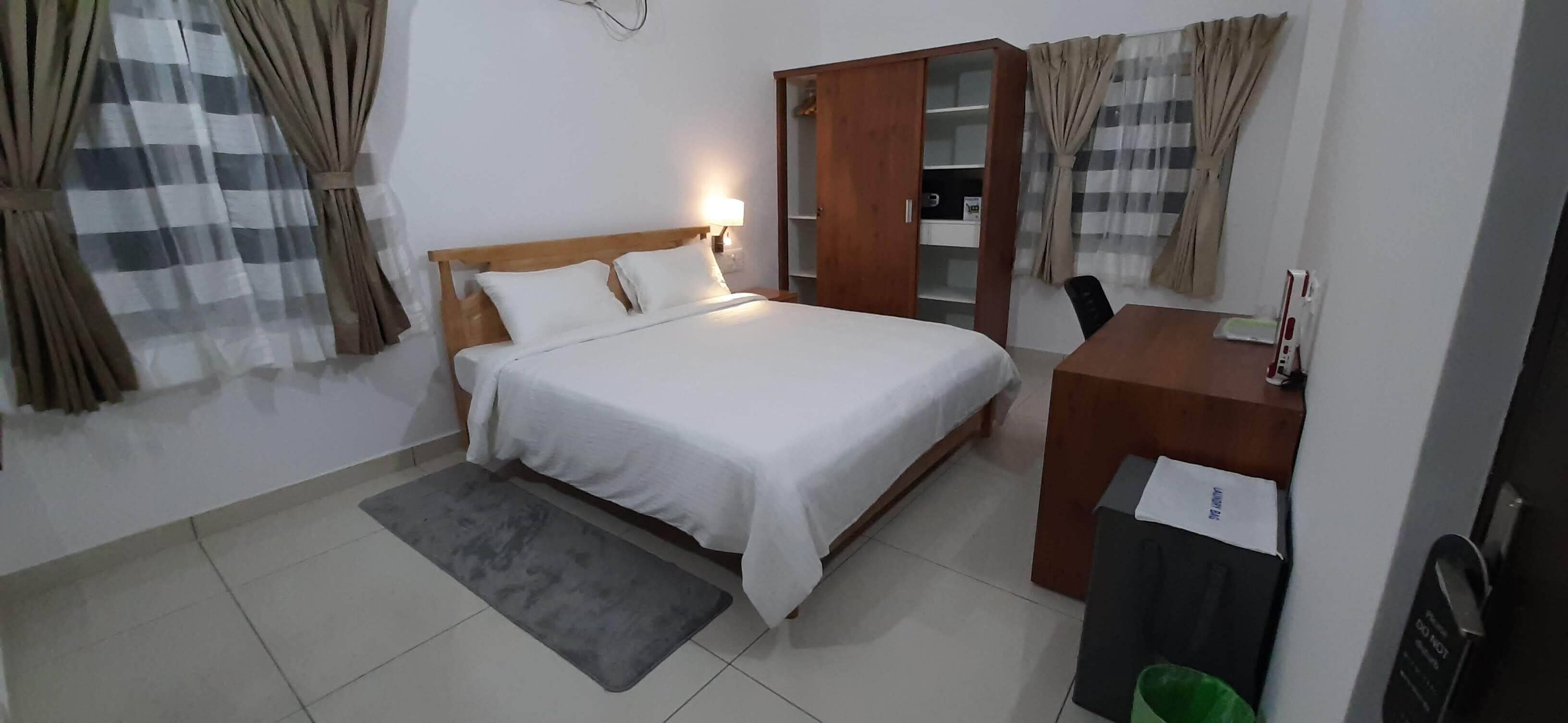 A neatly arranged bedroom with a bed, bedside table, wardrobe, and a desk with a chair.