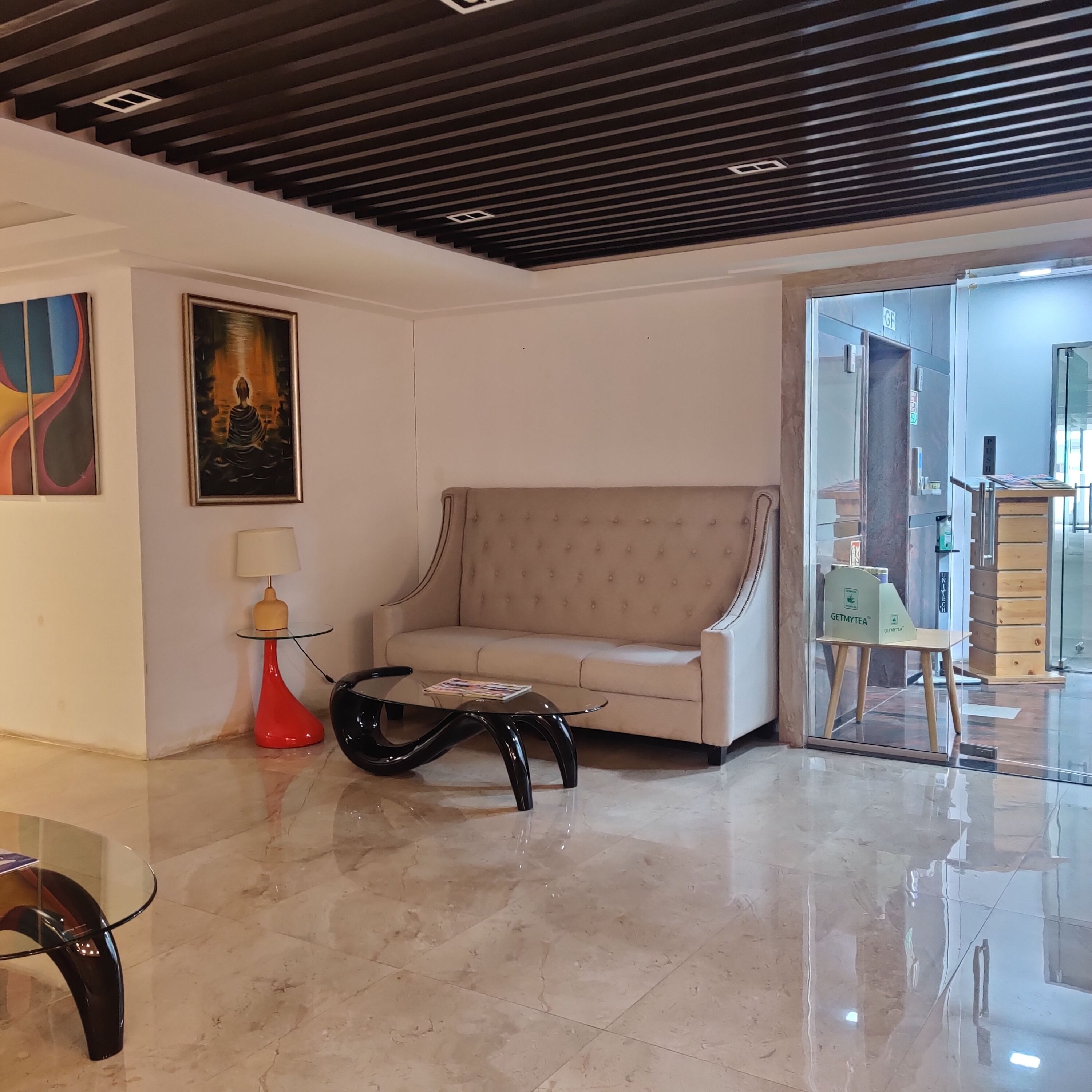 A modern living room with a beige sofa, a glass coffee table, and a red floor lamp.