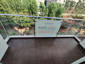 A balcony with a glass railing overlooking a garden with various trees and a sign advertising a hotel. - Senri By Yuhi (Tada)