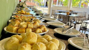 Montaje de bufé con diversos alimentos y platos, un área de estar al aire libre cubierta y vista a palmeras.