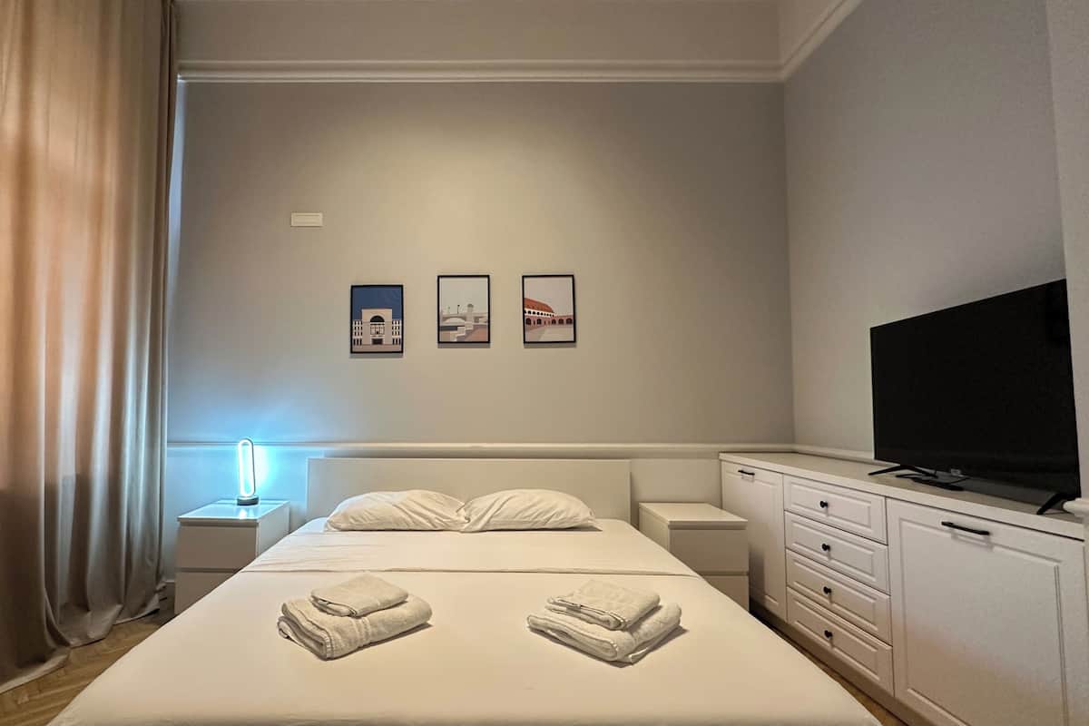 Habitación de hotel con cama, televisión, mesita de noche con lámpara y tres cuadros en la pared.