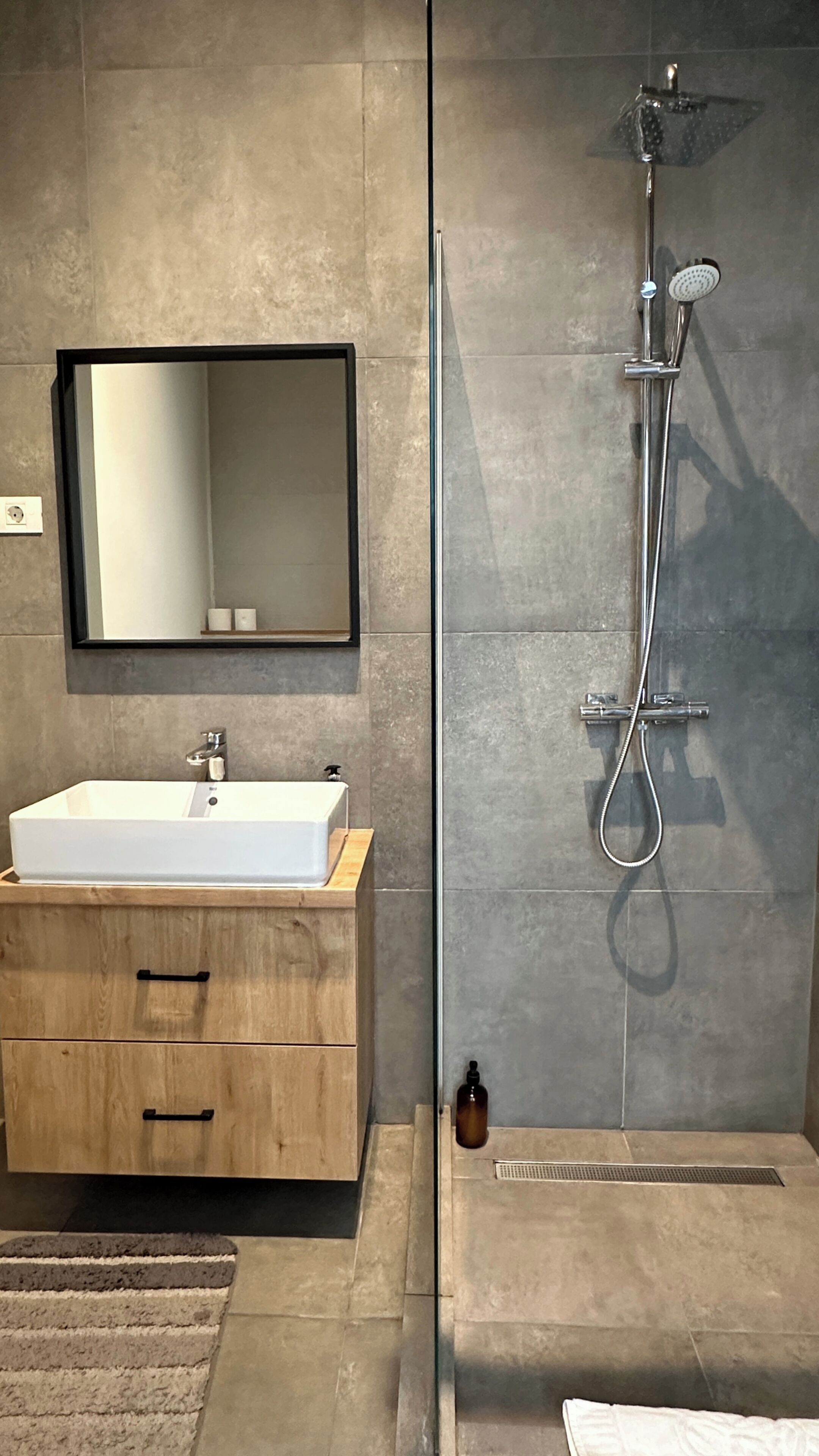 A modern bathroom with a rectangular sink, a mirror above it, and a shower with a handheld showerhead.