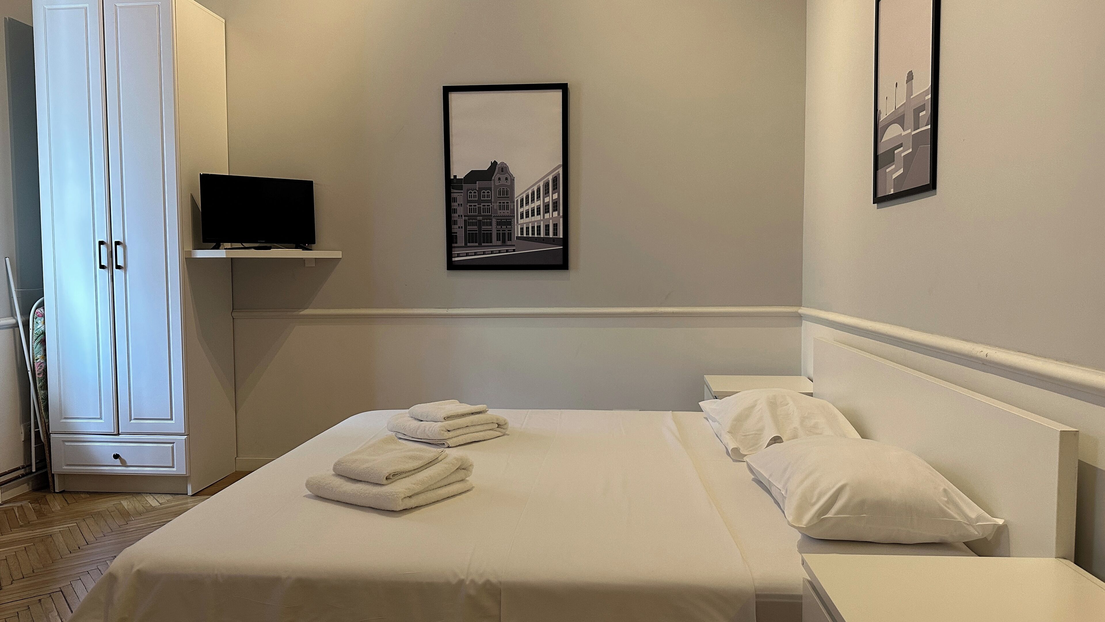A hotel room with a bed, a television on a shelf, and a framed picture on the wall.