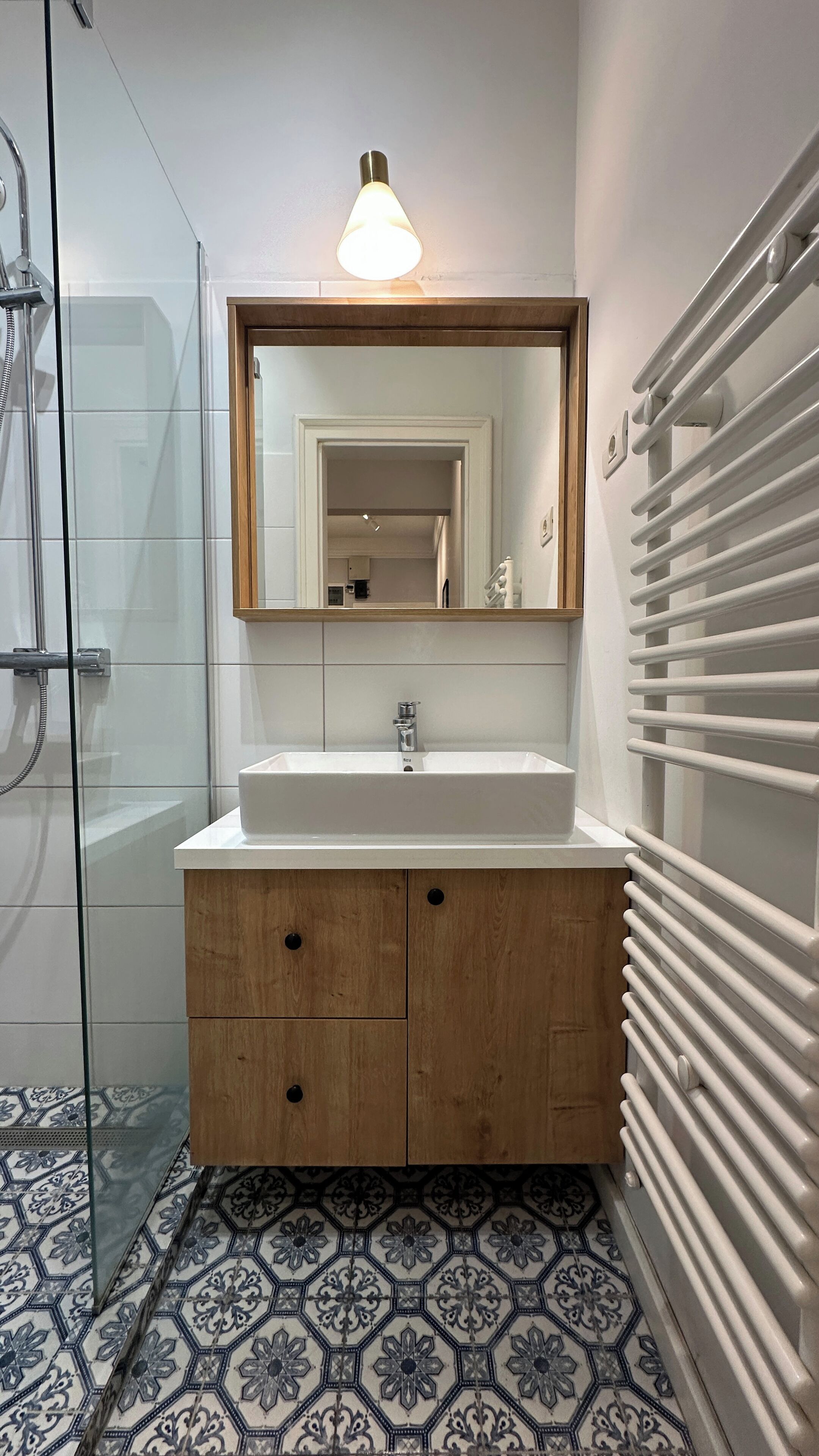 A bathroom with a glass shower enclosure, a wooden vanity with a white sink, and a mirror above it.