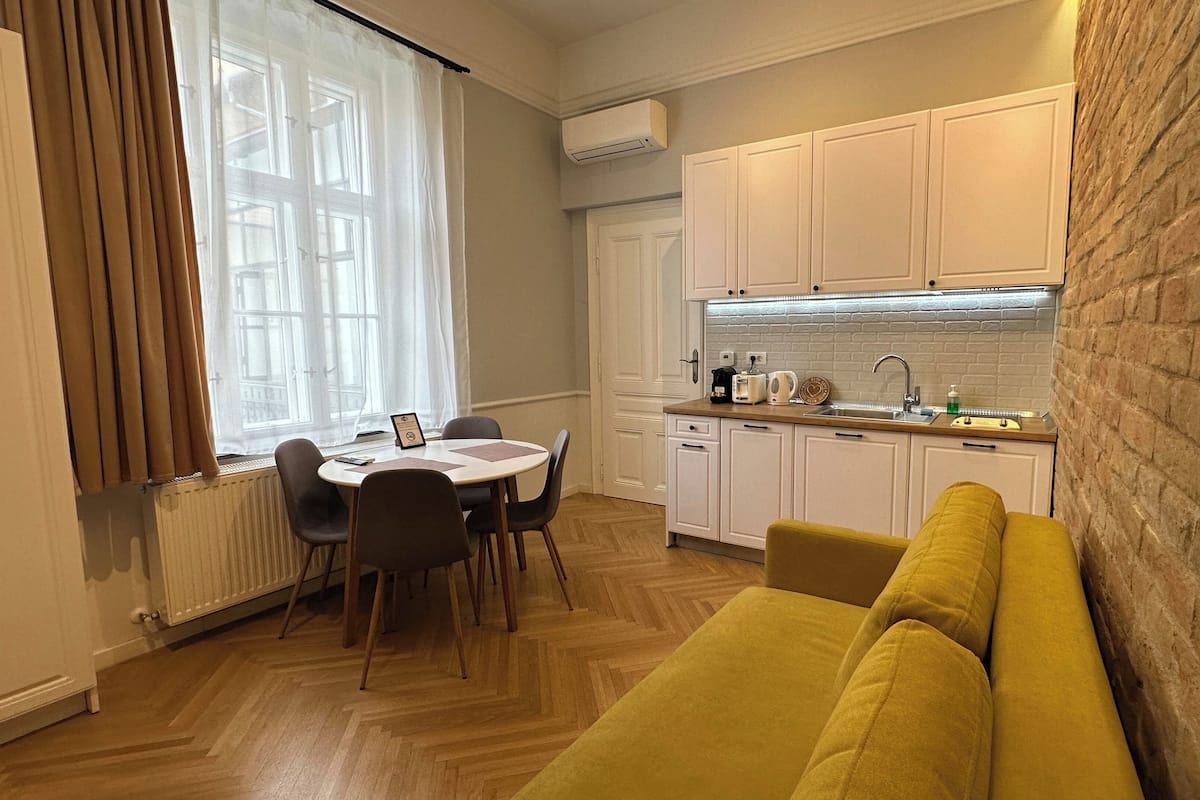 Una cocina compacta con armarios blancos, horno empotrado y ventana con cortinas traslúcidas.