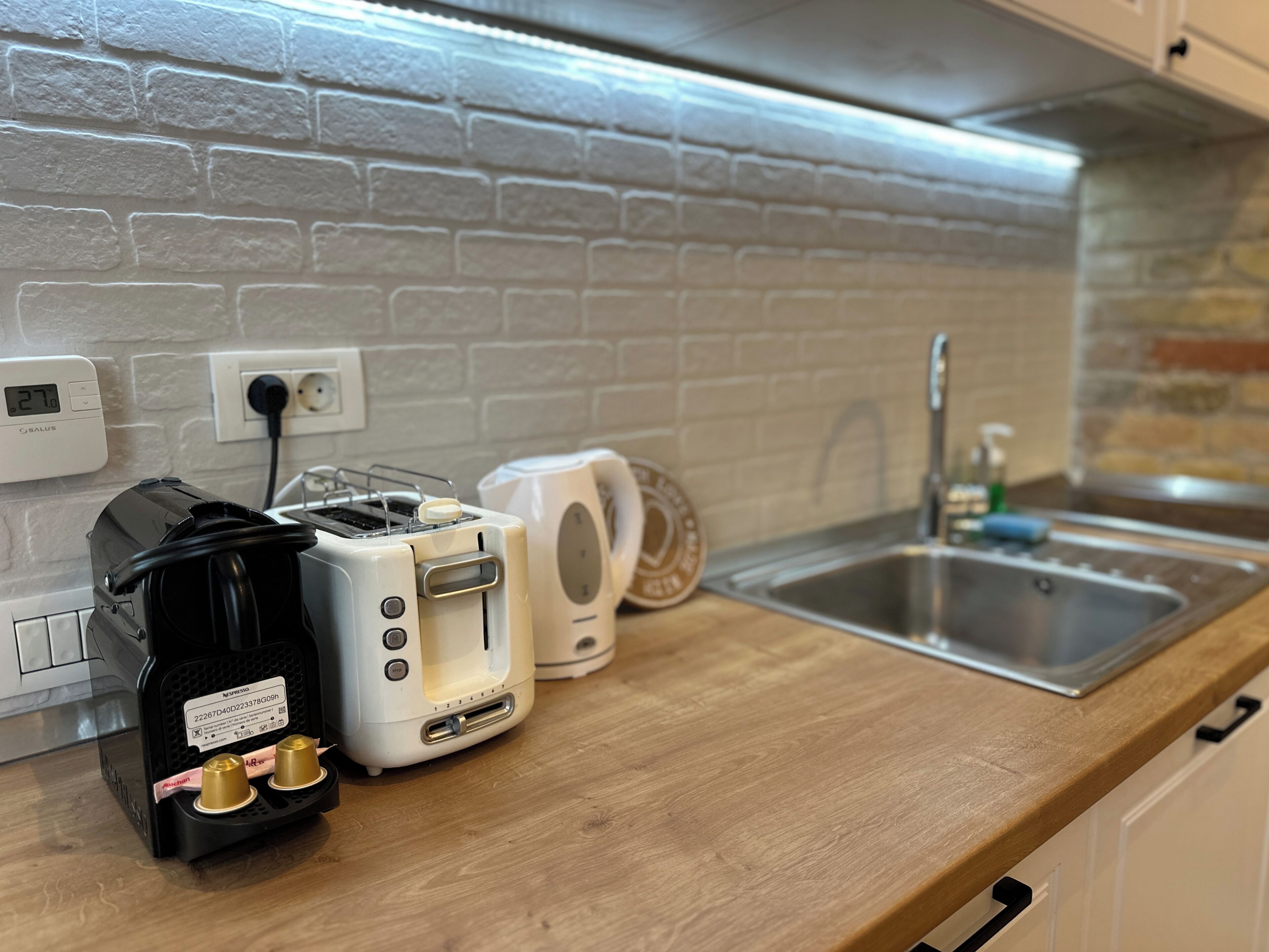 Una cocina con pared de ladrillo, un lavamanos, un tostador y una cafetera.