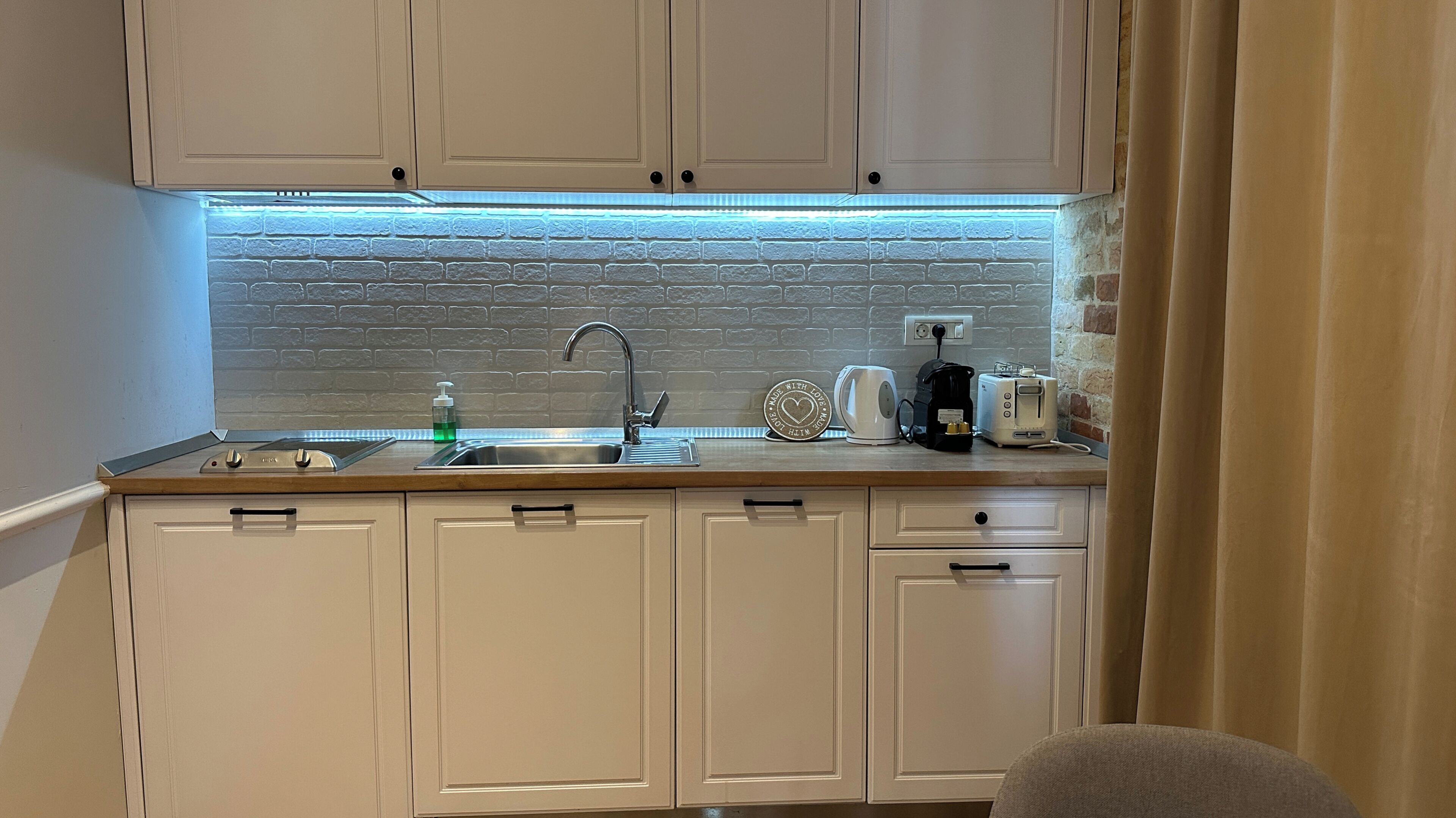 A compact kitchen with white cabinets, a stainless steel sink, a coffee maker, and a toaster.