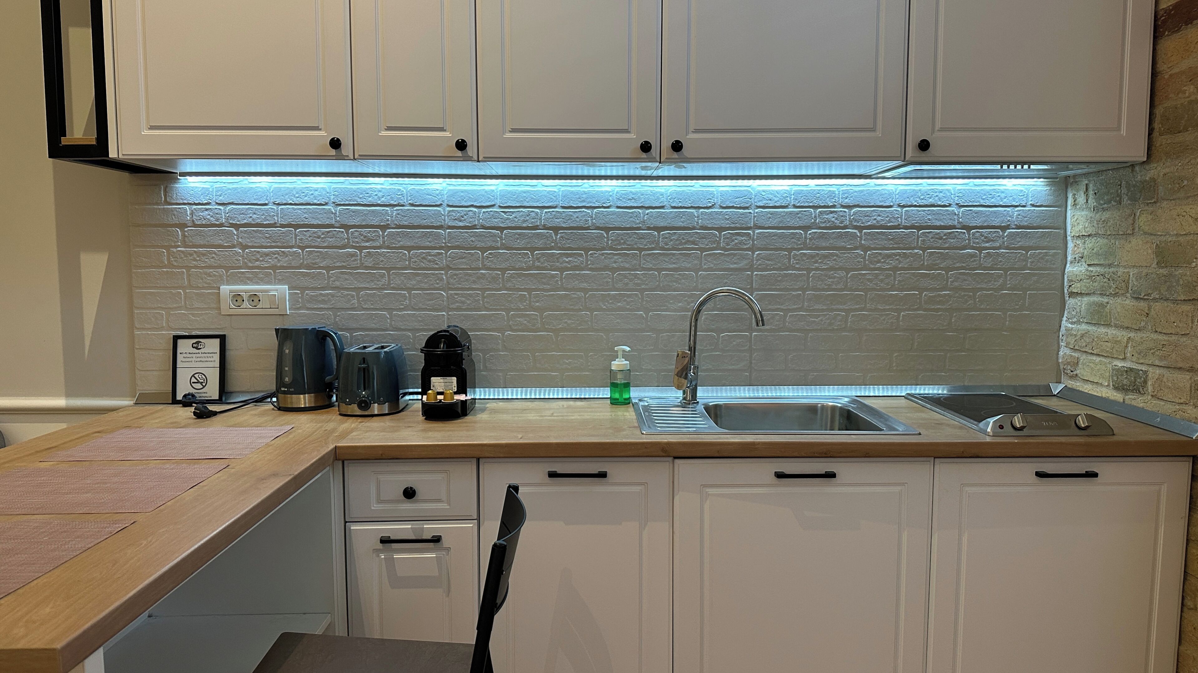 A compact kitchen with white cabinets, a brick backsplash, a sink, and various appliances.