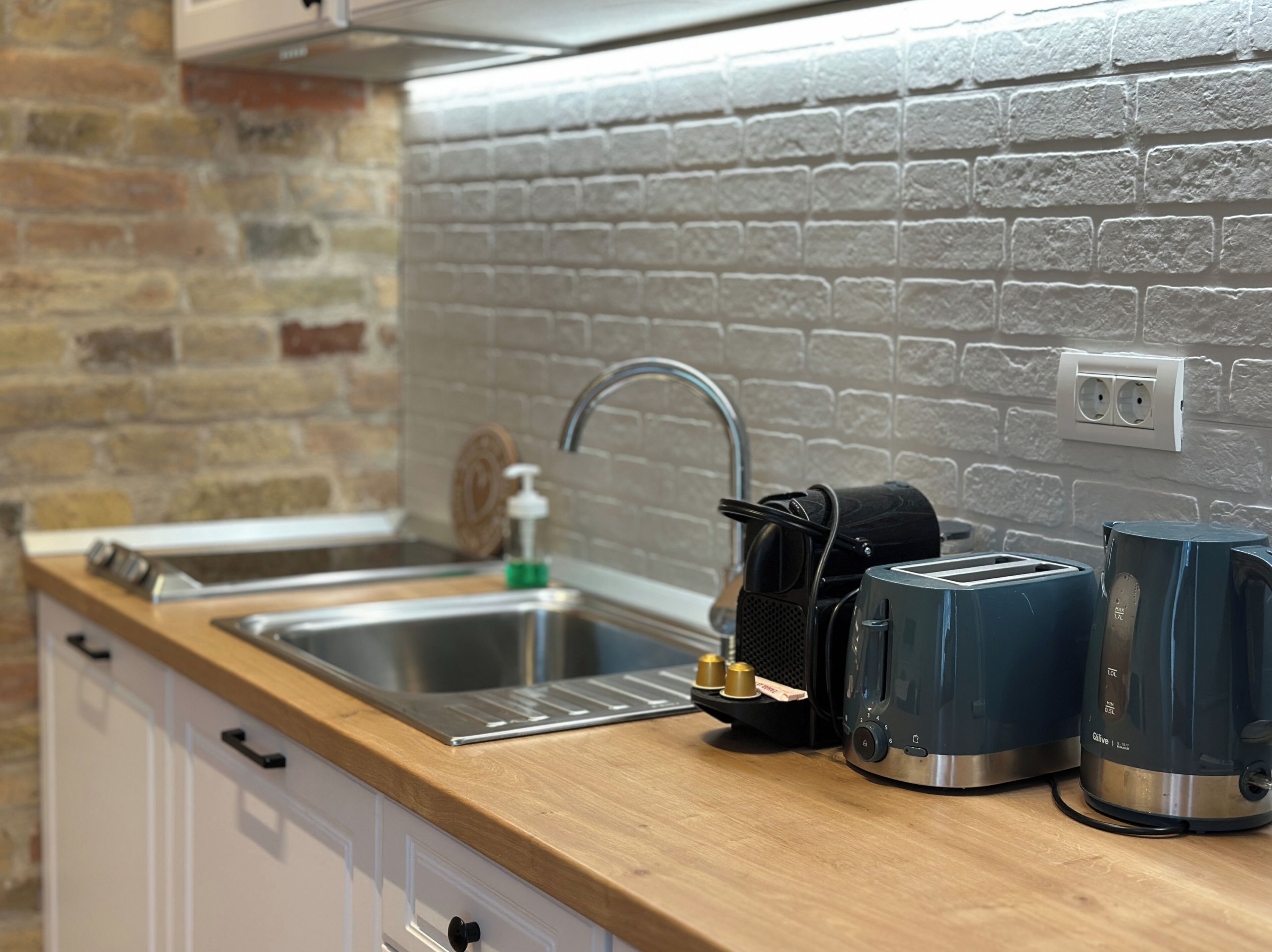 A kitchen with a brick wall, stainless steel sink, and a wooden countertop.