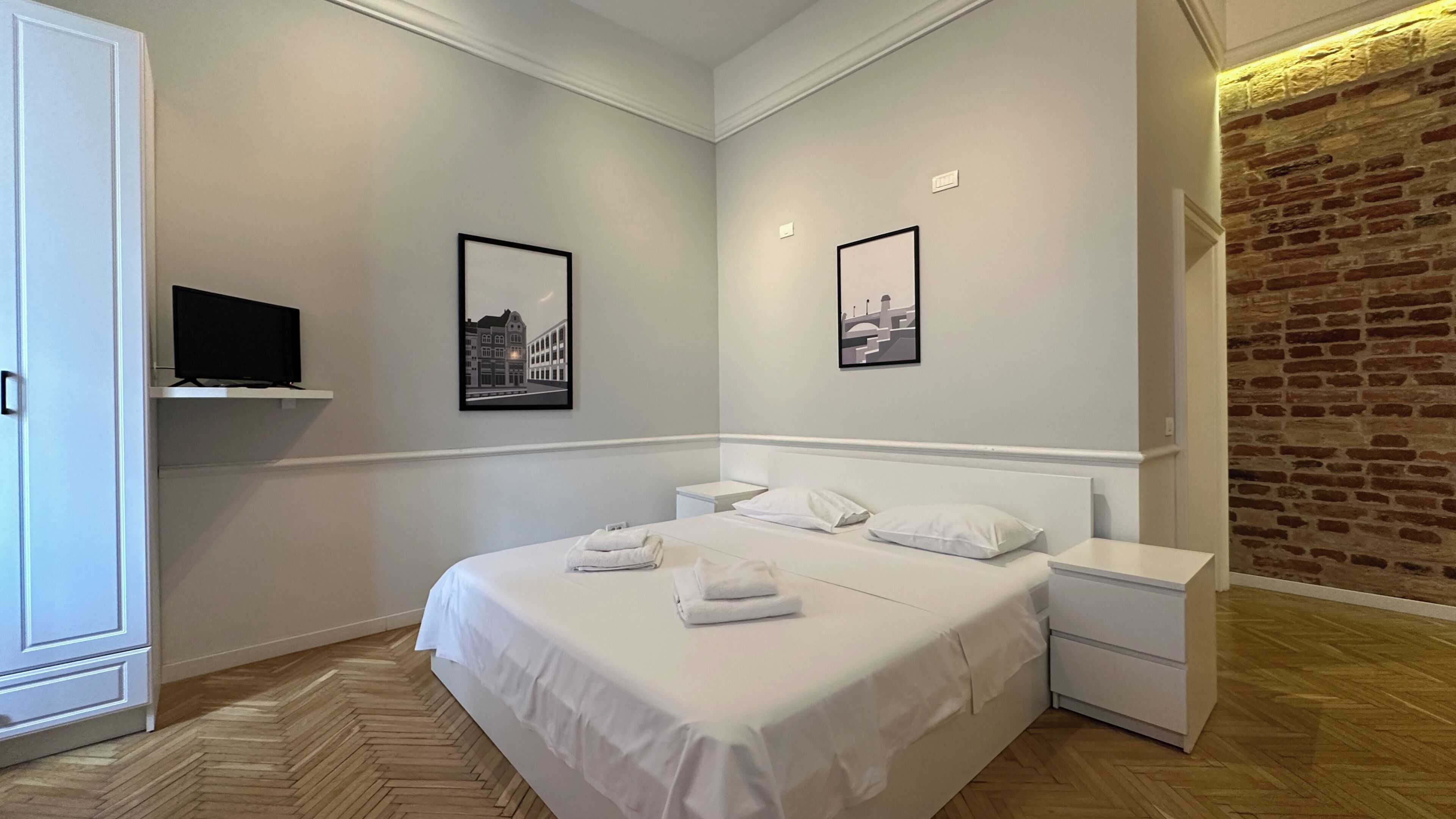 Een hotelkamer met een bed, twee nachtkastjes, een flatscreen televisie aan de muur en twee ingelijste foto's.
