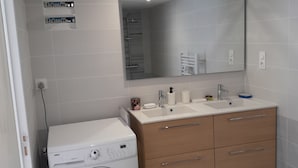 A modern bathroom with a built-in washing machine, a vanity with a mirror, and a sink. - Maison Chaleureuse au Calme Proximités Commodités (Montaigu-Vendée)