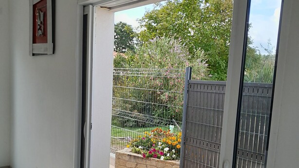 A room with a sliding glass door leading to an outdoor area with a garden and a metal fence. - Maison Chaleureuse au Calme Proximités Commodités (Montaigu-Vendée)
