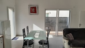 A modern living room with a glass-top dining table, black chairs, a white sofa, and a sliding glass door leading to a balcony. - Maison Chaleureuse au Calme Proximités Commodités (Montaigu-Vendée)