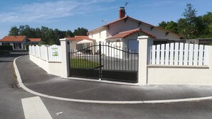 Een omheind woongebied met een wit huis, voorzien van een rode pannendak, een zwart metalen hek en een witte picket-omheining.
