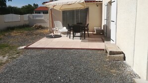 Een terras met een tafel en stoelen, een overdekt gedeelte met een parasol, en een witte deur.