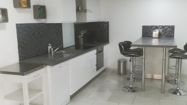 Een moderne keuken met witte kasten, een zwart aanrecht en een kleine eethoek met twee krukken.