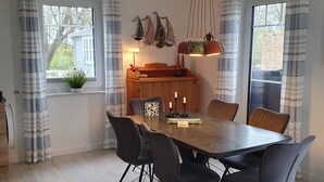 Un comedor con mesa de madera y sillas negras, un piano y una lámpara colgante.